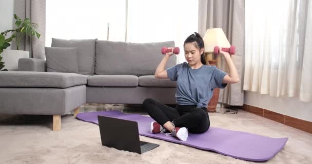 在客厅里用哑铃做运动 在笔记本电脑上看健身视频辅导 在家里做运动 在网上上健身课 健康的生活方式 — 图库视频影像