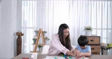 Mutlu Asyalı anne ve küçük oğlu birlikte resim yapıyorlar. Mutlu anne ve kız evde çizim yaparken eğleniyorlar. Yaşam tarzı aile anı.