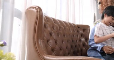 Mutlu Asyalı anne ve şirin oğlu evdeki oturma odasındaki kanepede okul ödevlerini yaparken internete bağlı tablet kullanıyor. Küçük bir çocukla Millennial ve birlikte eğleniyoruz..