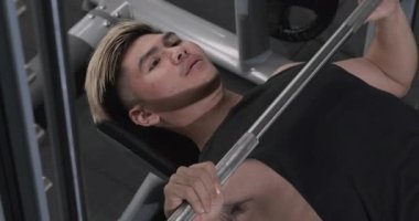 Koltukta halterle göğüs egzersizi yapan genç bir adam, spor yaşam tarzı ve sağlığı için spor motivasyonu, atletik vücut pozitifliği. Spor salonunda seçici odaklı Asyalı vücut geliştirici.