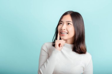 Diş teli takan genç Asyalı kadının diş telleri beyaz dişli güzel gülüşü mavi arka plandaki sağlığa olan güveni artırıyor izole edilmiş stüdyo çekimlerinde şaşırıyor ve fotokopi alanının tanıtımına seviniyor..