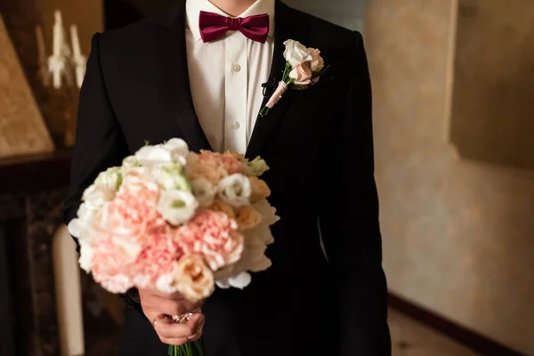 Close-up of a cropped frame is a tender bouquet of roses in the hands of a groom. Seorang pria dalam setelan pernikahan dengan dasi memegang bunga . — Stok Foto