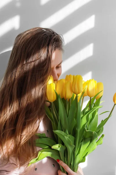 Woman with tulips. Young female with yellow flowers tulip natural portrait lifestyle near white background. Bouquet of yellow tulips for Birthday