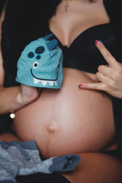 Cropped image pregnant woman holding hat for a baby in her hand and do rock symbol. Motherhood concept. Baby Shower — Stock Photo, Image