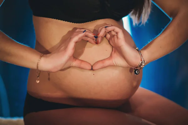Mujer embarazada sosteniendo el vientre, abrazando la barriga, haciendo símbolo de las manos del corazón en casa. Baby Shower. Concepto de maternidad . —  Fotos de Stock