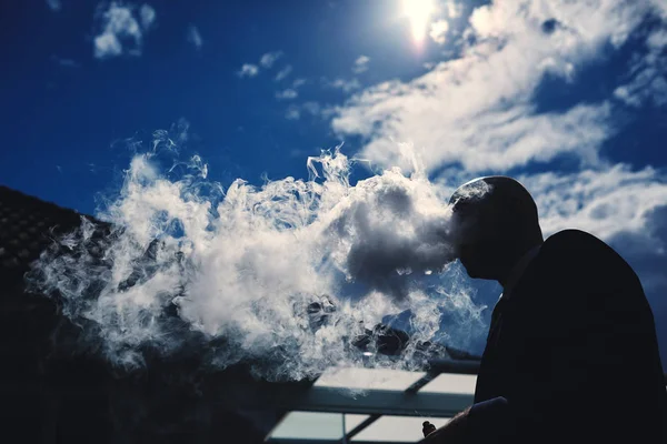 A man smokes a cigarette and releases a lot of smoke into the air. man smoke — Stock Photo, Image