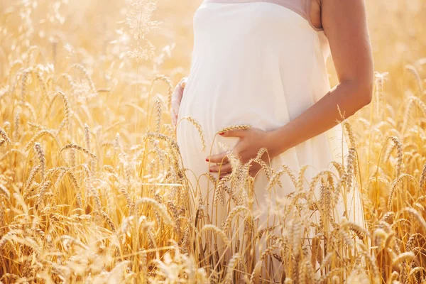 Schwangere in weißem Kleid auf einem Feld mit Koliken und Händchen auf dem Bauch. zugeschnittenes Foto aus nächster Nähe. Mutterschaftskonzept — Stockfoto