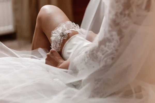 Woman wearing a garter on the leg. The bride holds in hand lose-up garter in hotel room. morning preparation wedding concept. — Stock Photo, Image