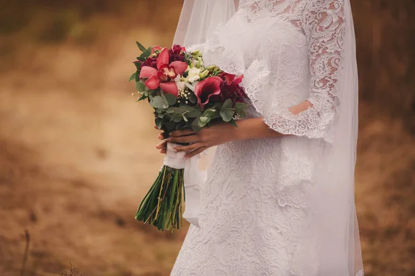 Jeune belle fille dans une robe élégante est debout et tenant bouquet de fleurs pastel et verts avec ruban à la nature . — Photo