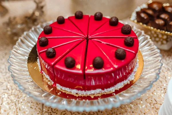 Pastel en esmalte rojo en la mesa, cortado en trozos. decorado con bolas de chocolate. barra de caramelo — Foto de Stock