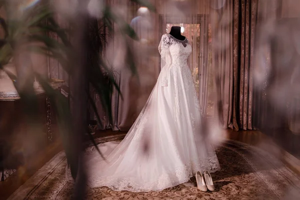 スタイリッシュで美しいウェディング ドレス。古典的なレース絹の結婚式のドレスは木造のホテルの部屋でハンガーに掛かっています。朝の準備結婚式のコンセプト. — ストック写真
