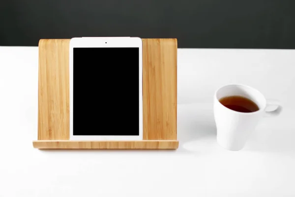 Tableta digital Mockup en soporte de madera. tableta en un soporte de madera. Taza blanca con té. lugar de trabajo —  Fotos de Stock