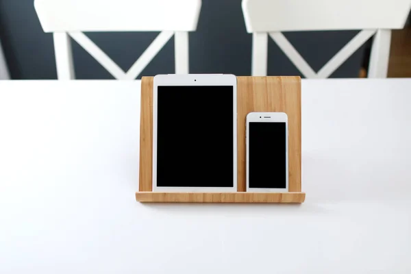 Um tablet branco e um smartphone com uma tela preta em um suporte em uma mesa branca. escritório local de trabalho — Fotografia de Stock