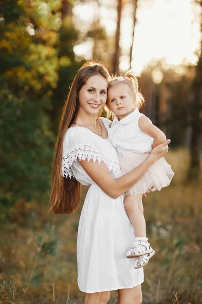 Portrait de mère et fille. Petite fille avec deux queues. mère tient une petite fille dans ses bras sur le fond d'une prairie — Photo