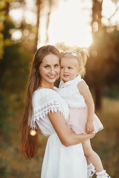 Petite fille avec deux queues. une femme tient un enfant dans ses bras dans le parc. jeune mère tenant sa petite fille dans ses bras alors qu'ils marchent dans le parc par une journée ensoleillée — Photo