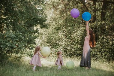 Anne ve iki kız el tutunup duruyor. Birlikte aile zamanı. Komik zaman. Balonlar olan kızlar. Yumuşak odaklama