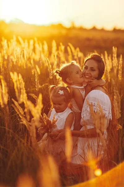 Anne ve iki kızı el ele tutuşuyorlar. Gün batımında birlikte aile zamanı. Neşeli piknik. Yumuşak odaklama.