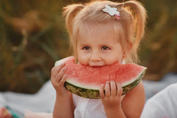 Child eating watermelon in the garden. Kids eat fruit outdoors. Healthy snack for children. Little girl playing in the garden holding a slice of water melon. Kid gardening