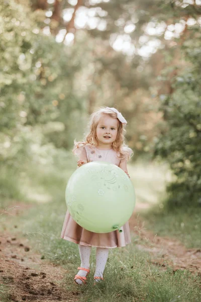 Stylish baby girl 4-5 year old holding big balloon wearing trendy pink dress in meadow. Playful. little girl with a balloon in the park. Birthday party. — Stock Photo, Image