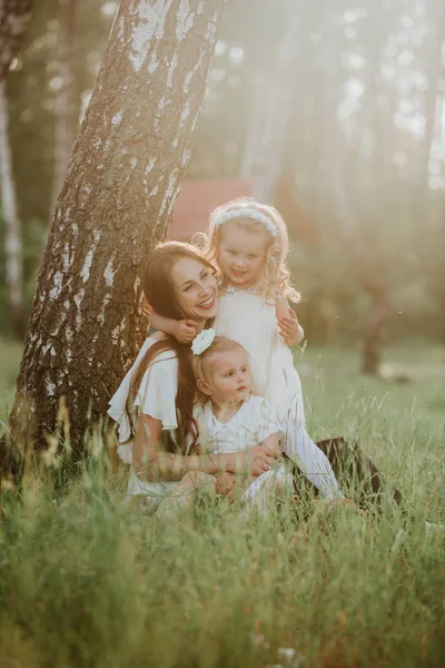 Famille joyeuse dans un parc, maman et leurs deux charmantes filles sont allongés sur l'herbe pendant qu'ils regardent la caméra — Photo