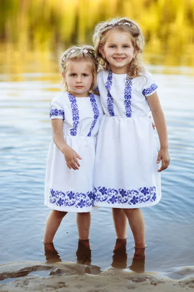 Two adorable little sisters laughing and hugging on warm and sunny summer day. two sisters in white dresses near the water.
