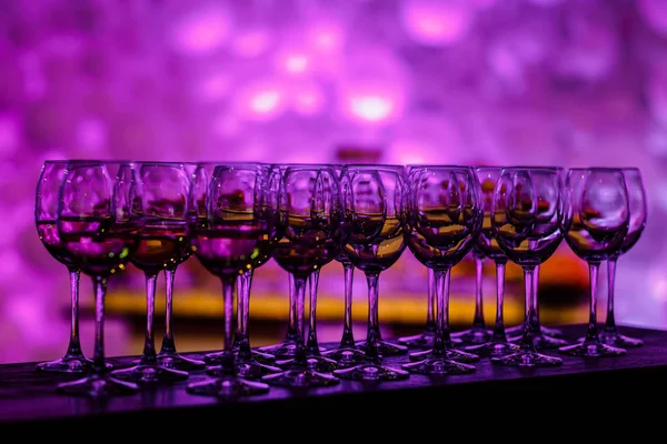 Geschirr in violettem Licht. viele Gläser Wein auf einem Tisch. Gläser mit Wein. gefüllt mit der Hälfte und stehen auf dem Tisch. Möbel. Selektiver Fokus — Stockfoto