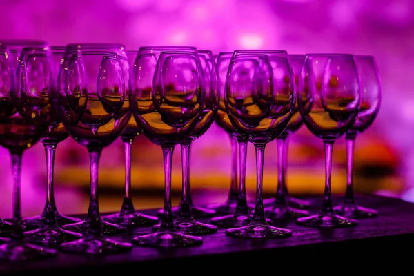Geschirr in violettem Licht. viele Gläser Wein auf einem Tisch. Gläser mit Wein. gefüllt mit der Hälfte und stehen auf dem Tisch. Möbel. Selektiver Fokus — Stockfoto