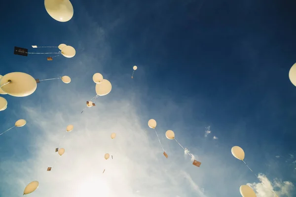 White balloons fly up into the blue sky. The release of festive balloons in the clouds. Celebration and happiness. Air gel balls in the atmosphere. — Stockfoto