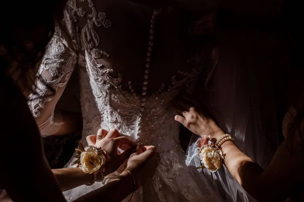 Bridesmaid helping bride fasten corset and getting her dress, preparing bride in morning for the wedding day. — Stock Photo, Image