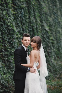 Romantik mutlu çift yeni evliler, gelin ve damat standları ve pembe ve mor çiçek ve yeşillik buket tutan, bahçede kurdele ile yeşillik. Doğa üzerine düğün töreni.