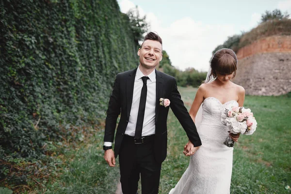 Casal atraente recém-casados está andando de volta em um trilho. Momento feliz e alegre. noiva e noivo abraçando no jardim florescendo primavera. belo buquê — Fotografia de Stock