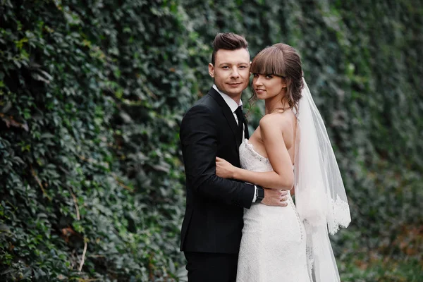 Elegante coppia di sposi il giorno del loro matrimonio. Felice giovane sposa, elegante sposo e bouquet da sposa. Ritratto di giovane coppia di sposi a natura . — Foto Stock