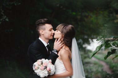 Gelin ve damat bir parkta öpüşme.çift yeni evli gelin ve damat doğa yeşil ormanda bir düğünde fotoğraf portre öpüşme vardır. Düğün çifti. Newlyweds.