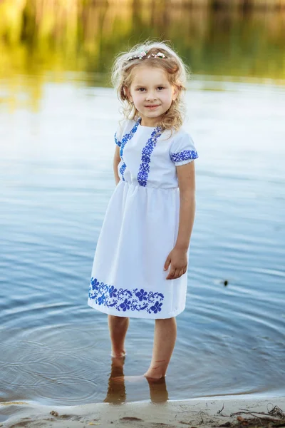 Portrét malé holčičky, která stojí ve vodě v bílých šatech. letní pláž. — Stock fotografie