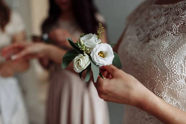 La novia sosteniendo en la mano de cerca las flores del ojal del novio con rosas blancas, y verde y verde. Preparativos para la novia. Concepto de boda . — Foto de Stock