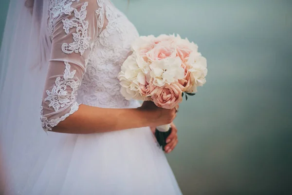 La mariée dans une élégante robe de mariée tient un beau bouquet de différentes fleurs et feuilles vertes. Thème mariage — Photo