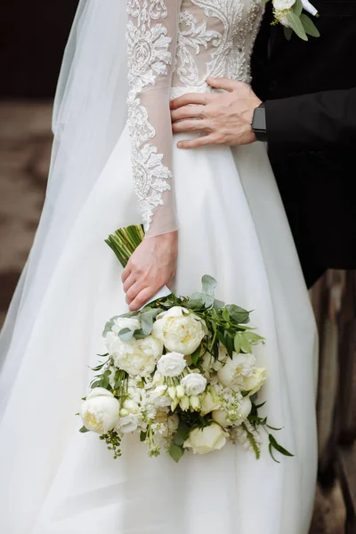 La novia en un vestido de novia elegante tiene un hermoso ramo de diferentes flores y hojas verdes. Tema de boda — Foto de Stock