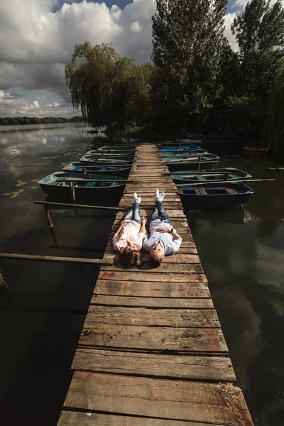 Güzel genç çift göl üzerinde ahşap bir köprü üzerinde yatıyor, sevgiyle birbirlerine bakar ve gülümsüyor. Aşk hikayesi. Sevgi dolu çift. — Stok fotoğraf