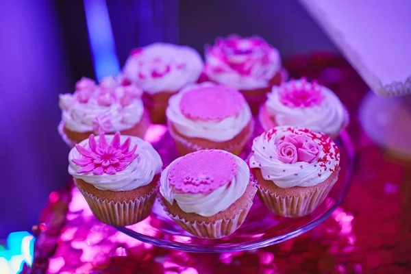 Набор вкусных вкусных кексов на праздничном фоне стола с блестящей розовой скатертью. Различные десертные тарталетки с декоративными кремами и розовыми декорациями. Выборочный фокус. Концепция Candy bar — стоковое фото