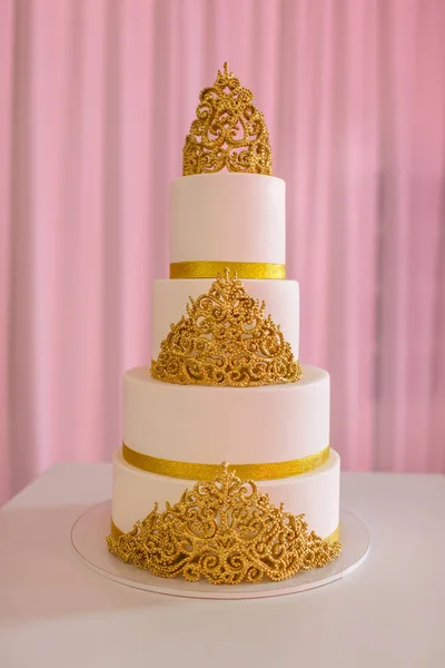 Svatební dort, na bílém stole. 3 vrstvy pokryté ve slonovině hmota se stříkající perličkami a Zlaté růže vyrobené z cukrové pasty. svatební dort se zlatem — Stock fotografie