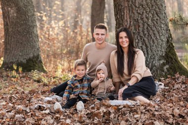 Mutlu, genç bir aile ve iki küçük çocuk güneşli bir günde sonbahar parkında rahatlıyor ve eğleniyorlar..
