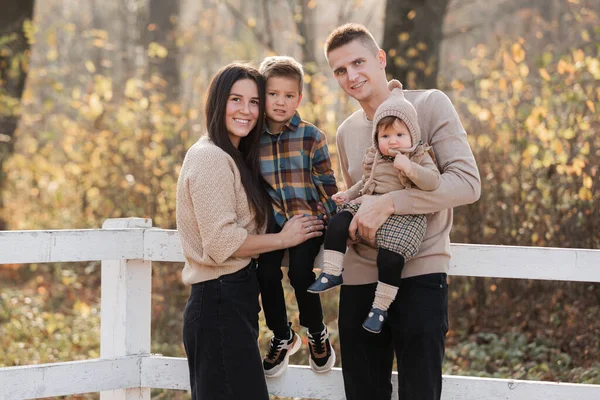 young dad and mom with baby girl and little son walking in autumn park on sunny day. happy family concept. mother's, father's, baby's day.