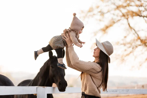 Jonge moeder en klein meisje in de buurt van een paard in de herfst zonnige dag. Moeder streelde een paard en glimlachte. Moederdag. — Stockfoto