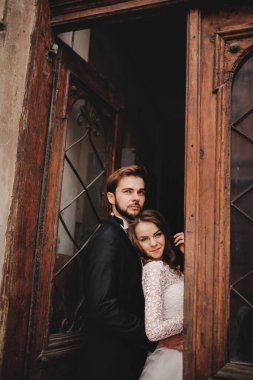 Güzel yeni evliler antik kapının yanında sarılıyorlar. Şık bir damadın düğün portresi ve Avrupa 'da eski bir evin yakınında genç bir gelin..