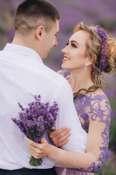 在夏天的阴冷的日子里 年轻夫妇在薰衣草地里拥抱和散步 穿着华丽的紫色衣服 发型和花束的女孩 — 图库照片