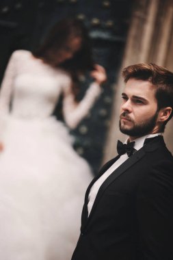 Eski yeşil kapının yanında bir düğün çifti var. Eski kasabanın arka planında taş duvarlar. Uzun saçlı, dantel elbiseli, damat takım elbiseli ve papyonlu gelin. Şefkatle sarıl. Romantik aşk.