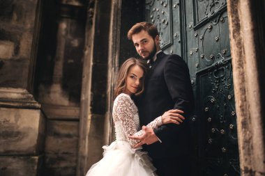 Eski yeşil kapının yanında düğün çifti kucaklaşması. Eski kasabanın arka planında taş duvarlar. Uzun saçlı, dantel elbiseli, damat takım elbiseli ve papyonlu gelin. Şefkatle sarıl. Romantik aşk