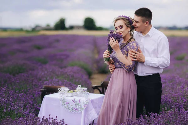 Young couple in love hugging in a lavender field on summer day. girl in a luxurious purple dress
