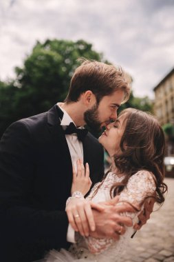 Eski Avrupa mahallesinde sarılıp öpüşen mutlu yeni evli çift, beyaz gelinlikli muhteşem gelin ve yakışıklı damat. düğün günü.