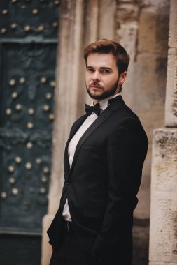 Eski bir Avrupa kasabasındaki şık genç bir damadın portresi. Eski binanın yanında papyonlu şık takım elbiseli bir adam. düğün günü.
